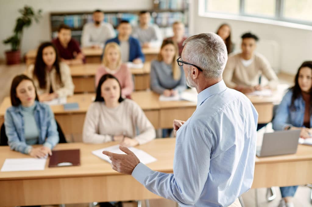 Back view of professor giving lecture to large group of students in the classroom