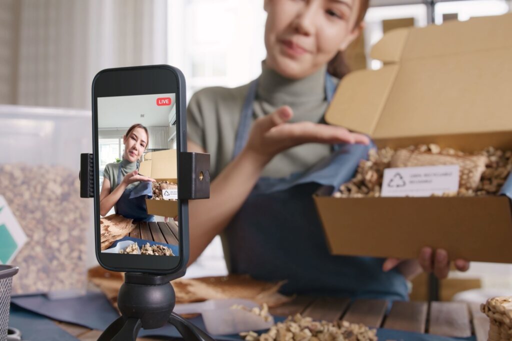 A woman films an unboxing video in front of a recording phone.