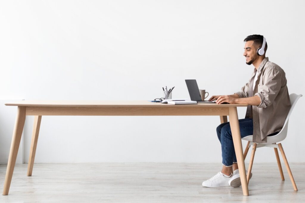 A freelancer sits at the end of a long table, using his laptop.